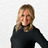 Paula from Baileys Hairdressing in Grantham, pictured with a bright, welcoming smile and soft, wavy blonde hair. Dressed in a classic black top against a clean neutral background, she radiates warmth, confidence and professional style.