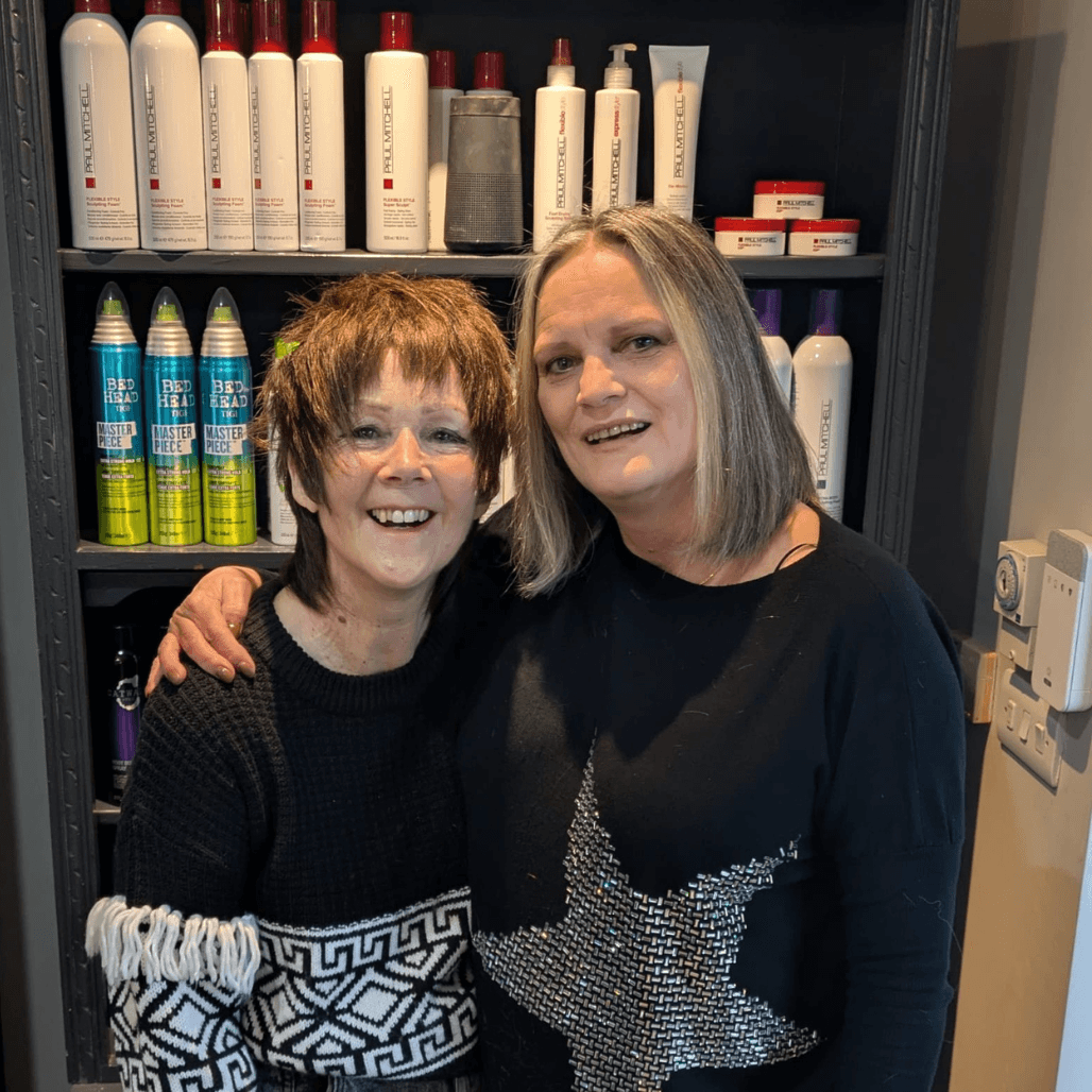 Jane from Baileys Hairdressing smiling with a happy client inside the Grantham salon, standing in front of professional hair products.
