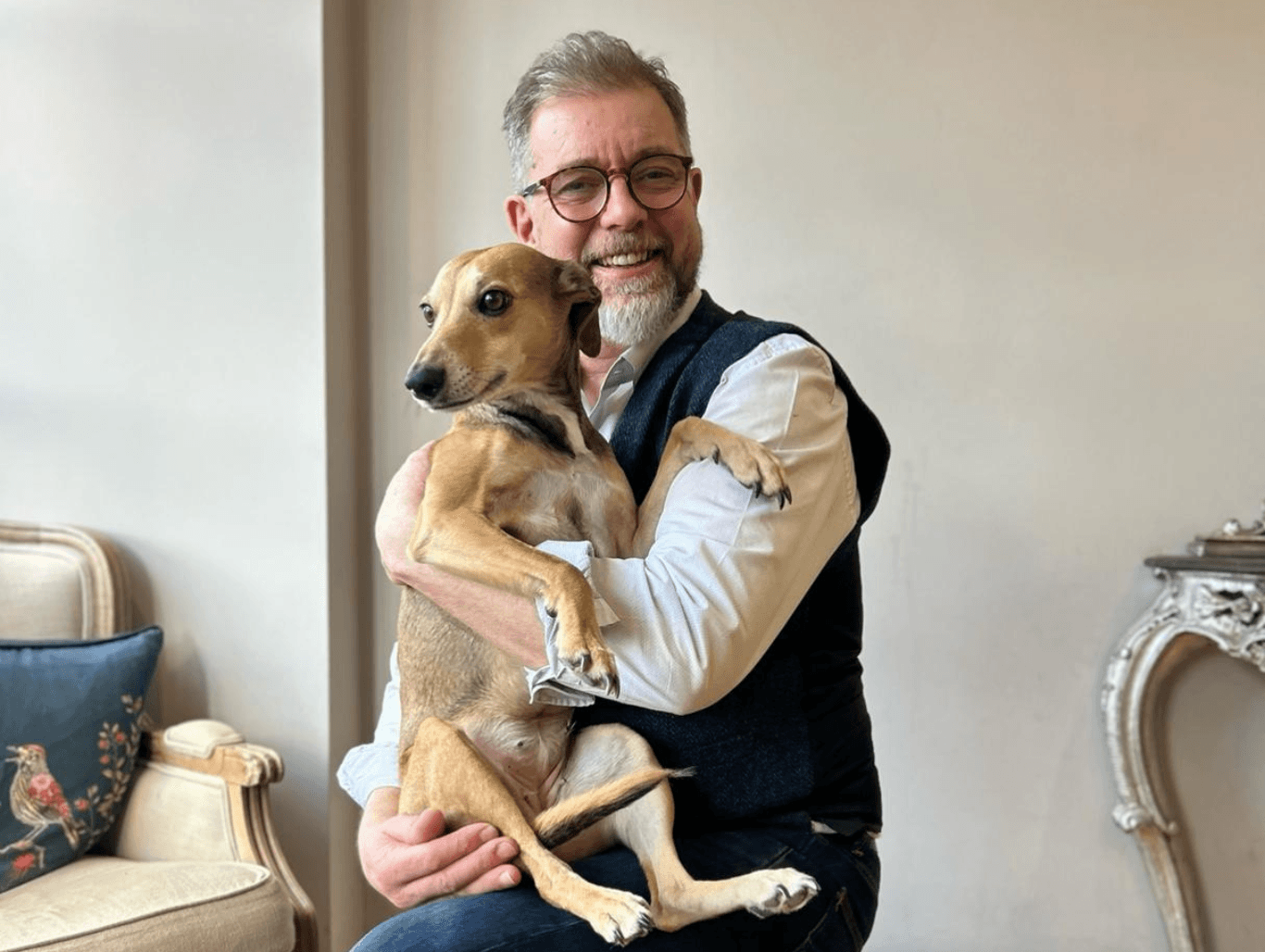 Simon from Baileys Hairdressing sitting in the salon holding the friendly salon dog, both smiling in a warm and welcoming setting.
