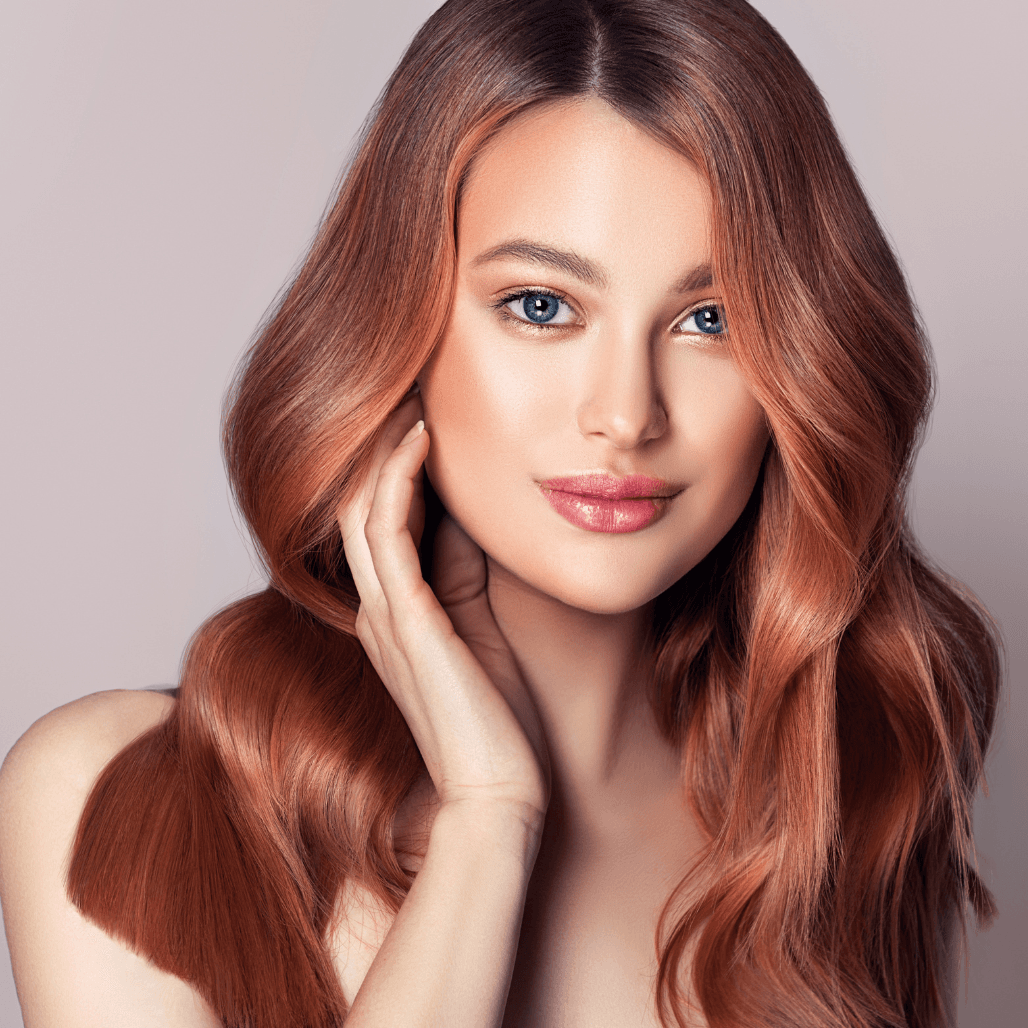 Striking woman with long, glossy copper-toned hair styled in soft waves, touching her face gently with a serene expression. A stunning showcase of professional blow-drying and colour work, reflecting the high-quality ladies’ cut and finish services at Baileys Hairdressing in Grantham.