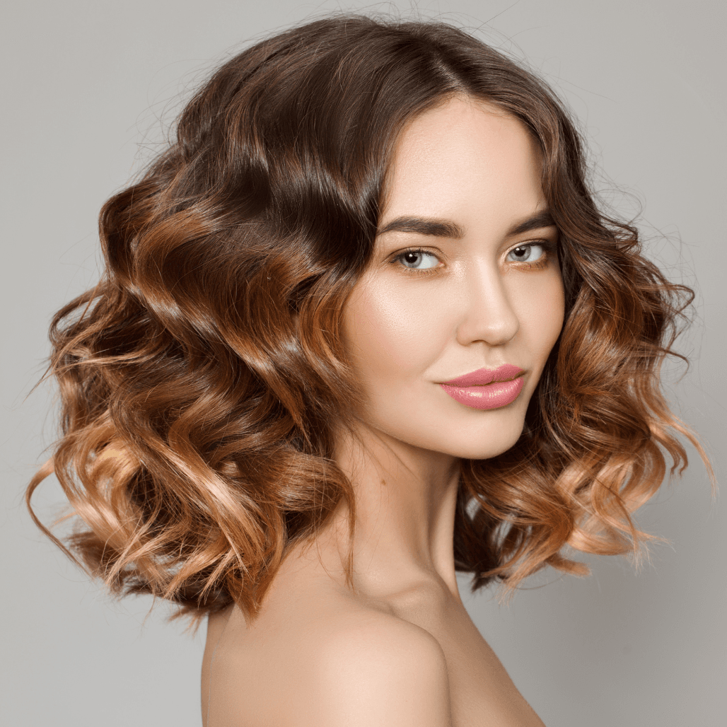 Woman with shoulder-length, voluminous brunette hair enhanced by soft caramel balayage highlights. Her glowing complexion and confident expression highlight the flawless finish of professional colouring services, perfectly capturing the difference between expert salon results and at-home DIY attempts — as delivered by Baileys Hairdressing in Grantham.